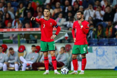 كريستيانو رونالدو يرتدي قميص منتخب البرتغال ويحتفل بهدف، مع خلفية ملعب كرة قدم.